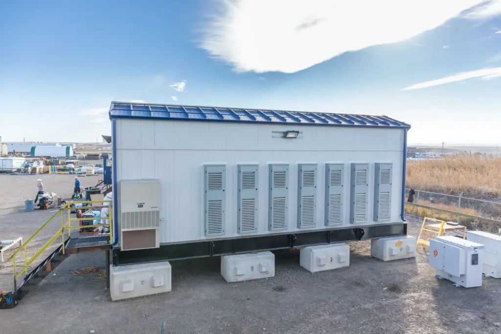 Tundra-built electrical building with ventilation louvres, set on blocks at a fabrication yard