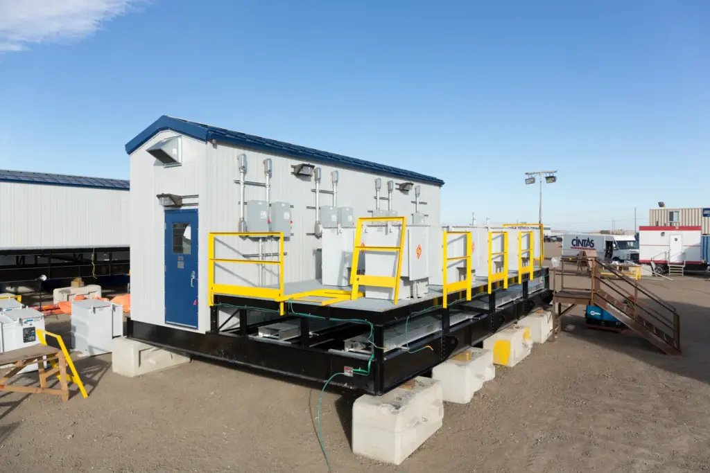 Skid-mounted electrical package with transformers on an open-grate deck and safety railings